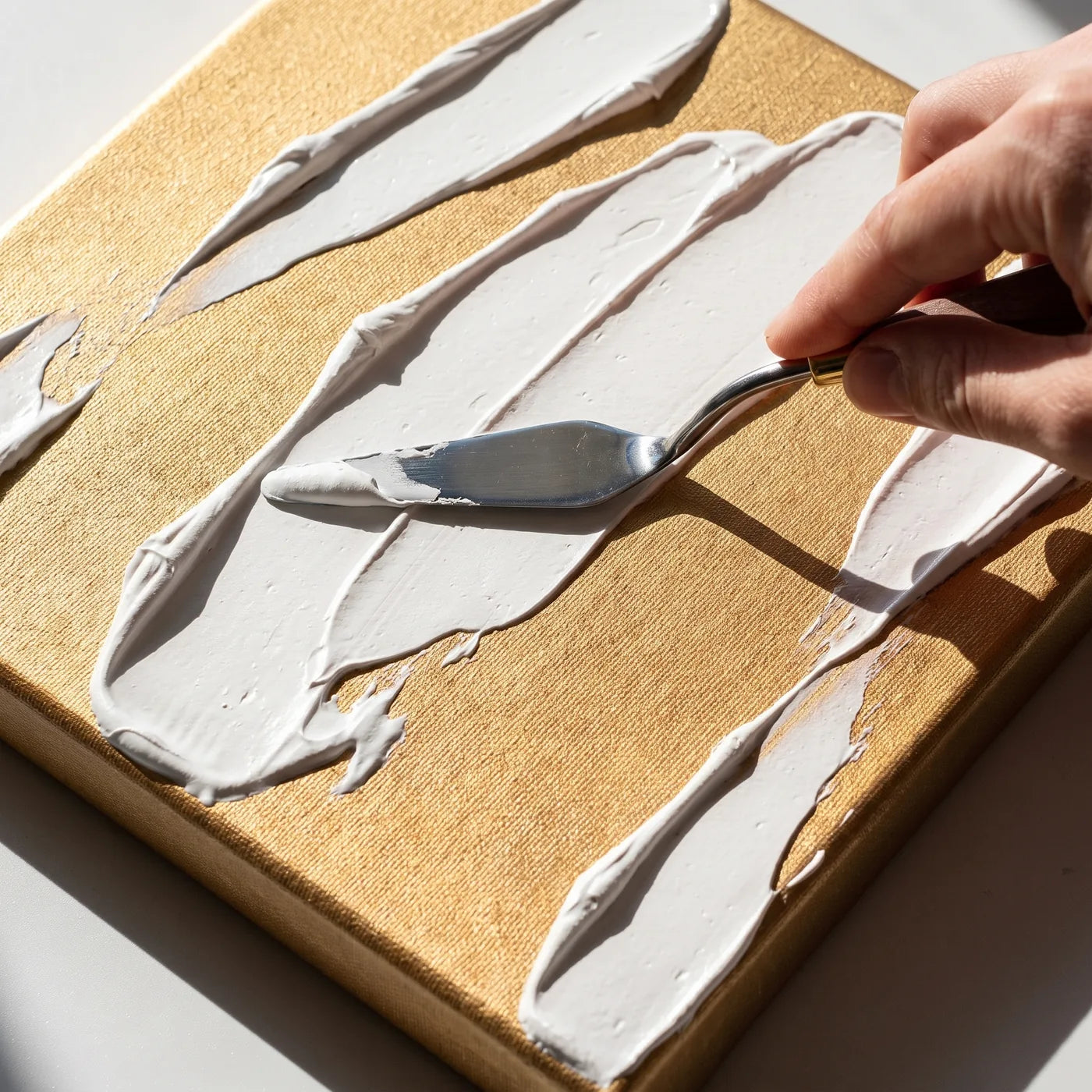 Pasta strutturante bianca stesa con la spatola sulla tela dorata MIDAS